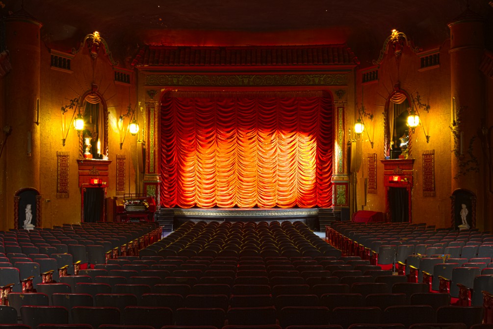 The main 700-seat auditorium with palazzo decor and dim lighting and a spotlight on the red velvet, waterfall curtain adorning the stage.