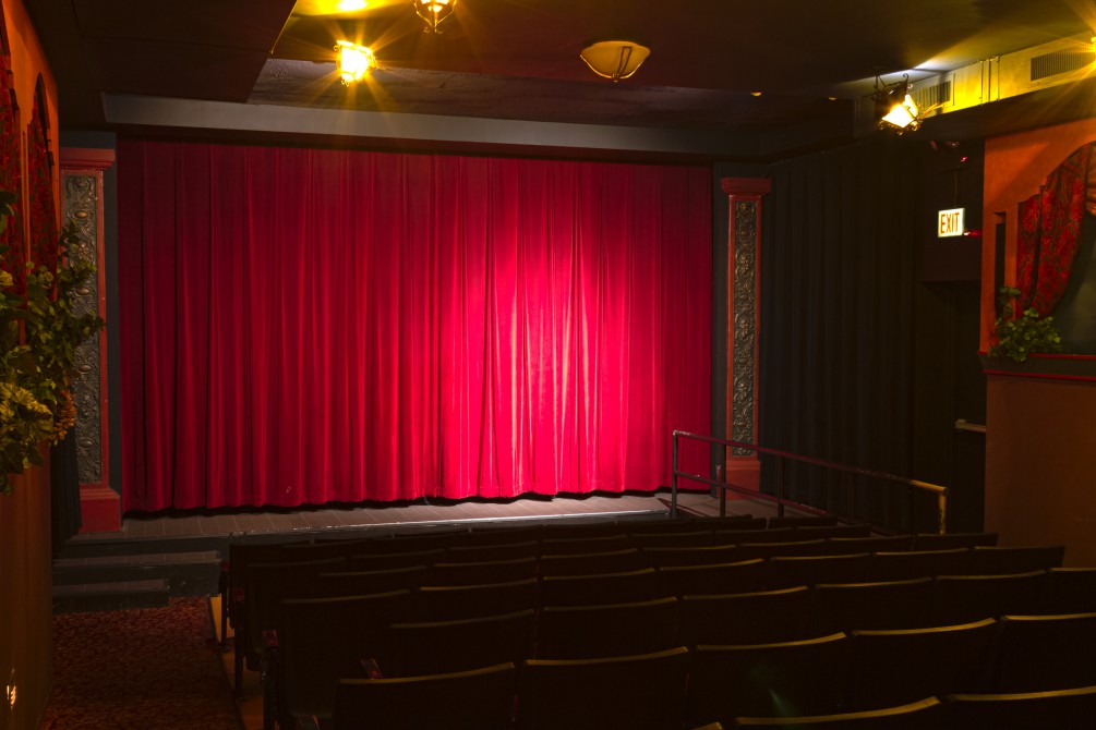 The more intimate setting of theatre two with fewer seats and better acoustics. It is dim light with a spotlight on the red velvet curtain that covers the screen.